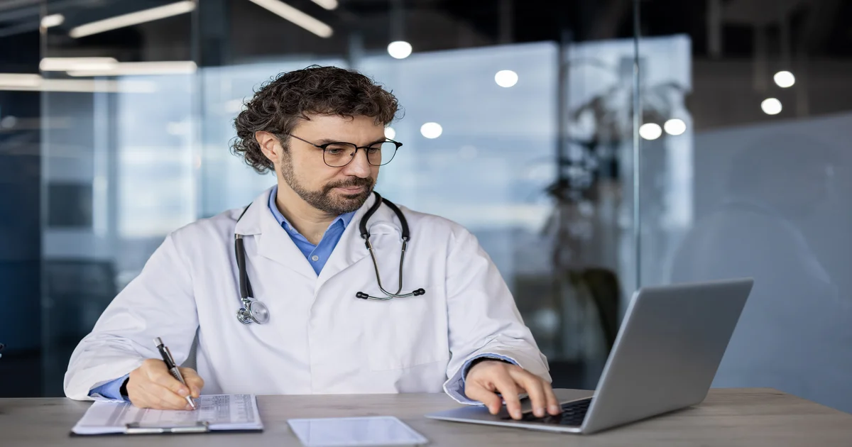 Médico focado trabalhando no laptop em clínica · cálculo do Fator R