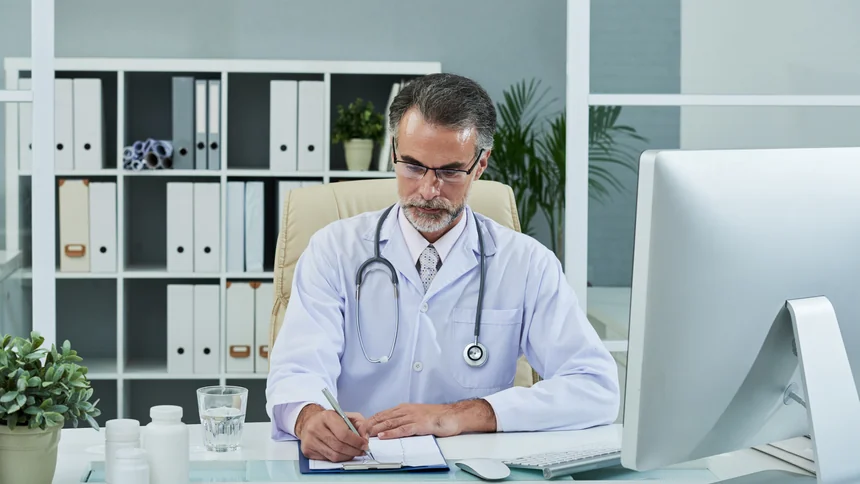 Médico PJ analisando gráficos de reforma tributária com calculadora e notebook